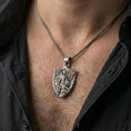 Load image into Gallery viewer, Oxidized Archangel Michael pendant with shield and sword worn on the neck in a lifestyle jewelry shot, styled against the chest for a bold and protective look