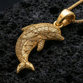 Load image into Gallery viewer, Gold plated dolphin pendant necklace presented on porous volcanic rock, highlighting the patterned surface in a luxurious close-up jewelry image.