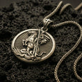 Load image into Gallery viewer, Bronze Saint George pendant with mounted warrior relief, spear detail, and round medallion design displayed on dark volcanic rock in a close-up luxury jewelry composition