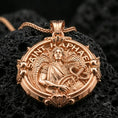 Load image into Gallery viewer, Gold plated Saint Raphael necklace with winged healer motif, serpent staff detail, and circular devotional design showcased on black volcanic rock in a refined macro jewelry image
