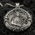 Load image into Gallery viewer, Oxidized Saint Raphael pendant with winged archangel figure, healing staff with serpent, and Saint Raphael inscription displayed on dark volcanic rock in a close-up luxury jewelry composition