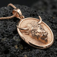 Load image into Gallery viewer, Rose gold plated bull pendant necklace on dark volcanic rock, photographed in a detailed premium studio macro view.