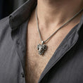 Load image into Gallery viewer, Oxidized ram head pendant necklace worn on the neck, styled in a dark lifestyle portrait with an open shirt and masculine presentation.