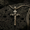 Load image into Gallery viewer, Bronze INRI crucifix pendant with sculpted Jesus figure and wood-textured cross displayed on dark volcanic rock in a close-up luxury jewelry composition
