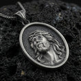 Load image into Gallery viewer, Oxidized Jesus Christ pendant with crown of thorns and detailed sacred portrait displayed on dark volcanic rock in a close-up luxury jewelry composition