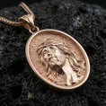Load image into Gallery viewer, Rose gold plated religious Jesus medal with detailed crown of thorns portrait and smooth oval silhouette resting on volcanic rock in an elegant close-up product presentation