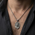 Load image into Gallery viewer, Oxidized Jesus Christ pendant with crown of thorns and radiant halo worn on the neck in a lifestyle jewelry shot, styled against the chest for a bold and devotional look