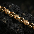 Load image into Gallery viewer, Gold plated evil eye link chain necklace presented on porous volcanic rock, highlighting the sculpted symbolic links in a luxurious close-up jewelry image.