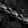 Load image into Gallery viewer, Sterling silver evil eye link chain necklace with an oxidized finish resting on textured volcanic rock, captured in a close-up premium studio composition.