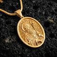 Load image into Gallery viewer, Gold plated Saint Patrick pendant necklace presented on porous volcanic rock, highlighting the oval medallion form and sacred devotional design in a luxurious close-up jewelry image.