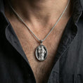Load image into Gallery viewer, Polished silver Saint Dominic medallion with robed saint relief worn on the neck in a close lifestyle frame, highlighting the oval silhouette and sacred inscription