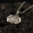 Load image into Gallery viewer, Bronze third eye chakra pendant with Om symbol, triangle motif, and two-petal lotus design displayed on dark volcanic rock in a close-up luxury jewelry composition
