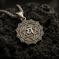 Load image into Gallery viewer, Bronze Anahata chakra pendant with sacred symbol, hexagram motif, and sunburst border displayed on dark volcanic rock in a close-up luxury jewelry composition