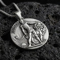 Load image into Gallery viewer, Oxidized Lion of Judah pendant with Judah inscription, lion figure, and sunrise motif displayed on dark volcanic rock in a close-up luxury jewelry composition