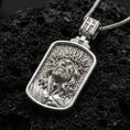 Load image into Gallery viewer, Polished silver Jesus medal with rounded rectangular frame, crown of thorns, and sculpted Christ portrait placed on textured volcanic rock in a premium studio product shot