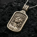Load image into Gallery viewer, Bronze Jesus Christ pendant with crown of thorns, framed sacred portrait, and detailed devotional relief displayed on dark volcanic rock in a close-up luxury jewelry composition