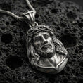 Load image into Gallery viewer, Oxidized Jesus Christ pendant with crown of thorns, sculpted sacred portrait, and detailed facial relief displayed on dark volcanic rock in a close-up luxury jewelry composition