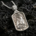 Load image into Gallery viewer, Polished silver Jesus medallion with rounded rectangular frame, detailed seated Christ portrait, and engraved geometric background placed on textured volcanic rock in a premium studio product shot