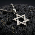Load image into Gallery viewer, Bronze Star of David pendant with interlocking geometric lines and open hexagram silhouette displayed on dark volcanic rock in a close-up luxury jewelry composition