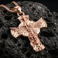 Load image into Gallery viewer, Rose gold plated Archangel Michael cross pendant with detailed wings, protective shield, and symbolic devil-defeating design resting on volcanic rock in an elegant close-up product presentation