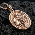 Load image into Gallery viewer, Rose gold plated crusader knight pendant with armored figure, sword detail, and oval devotional-medieval silhouette resting on volcanic rock in an elegant close-up product presentation