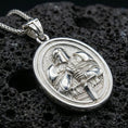 Load image into Gallery viewer, Polished silver crusader necklace with armored knight relief, oval frame, and detailed sword motif placed on textured volcanic rock in a premium studio product shot