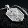 Load image into Gallery viewer, Polished silver Saint Michael shield pendant necklace displayed on black volcanic rock, shown in a refined macro product shot with detailed archangel relief and protective shield motif.