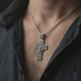 Load image into Gallery viewer, Oxidized Orthodox cross pendant necklace worn on the neck, styled in a dark lifestyle portrait with an open shirt and masculine presentation.