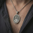 Load image into Gallery viewer, Oxidized Saint Michael Archangel pendant necklace worn on the neck, styled in a dark lifestyle portrait with an open shirt and masculine presentation.