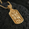 Load image into Gallery viewer, Gold plated Saint George dog tag pendant necklace presented on porous volcanic rock, highlighting the rectangular devotional form in a luxurious close-up jewelry image.