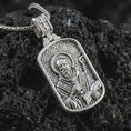 Load image into Gallery viewer, Polished silver Saint Benedict dog tag pendant necklace displayed on black volcanic rock, shown in a refined macro product shot with detailed saint figure, staff, book, and engraved background pattern.