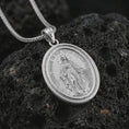 Load image into Gallery viewer, Polished silver Miraculous Medal pendant necklace displayed on black volcanic rock, shown in a refined macro product shot with detailed Virgin Mary figure and engraved prayer lettering.