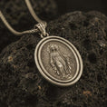 Load image into Gallery viewer, Bronze Miraculous Medal pendant necklace with an oxidized finish resting on textured volcanic rock, captured in a close-up premium studio composition.