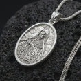 Load image into Gallery viewer, Polished silver Saint Rita pendant necklace displayed on black volcanic rock, shown in a refined macro product shot with detailed saint figure, crucifix, and floral relief.
