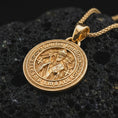 Load image into Gallery viewer, Gold plated Saint Benedict medal pendant necklace presented on porous volcanic rock, highlighting the round devotional medallion design in a luxurious close-up jewelry image.