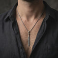 Load image into Gallery viewer, Oxidized Dragonslayer sword pendant necklace worn on the neck, styled in a dark lifestyle portrait with an open shirt and masculine presentation.