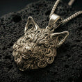 Load image into Gallery viewer, Bronze wolf head pendant with intricate carved fur details and fierce animal expression displayed on dark volcanic rock in a close-up luxury jewelry composition