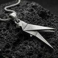 Load image into Gallery viewer, Oxidized origami parrot pendant with geometric folded bird form and sleek angular silhouette displayed on dark volcanic rock in a close-up luxury jewelry composition