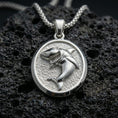 Load image into Gallery viewer, Polished silver shark necklace with detailed predatory shark design, oval pendant silhouette, and textured marine-style backdrop placed on textured volcanic rock in a premium studio product shot
