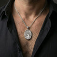 Load image into Gallery viewer, Polished silver peafowl necklace with detailed plumage and floral accents worn on the neck in a close lifestyle frame, highlighting the oval medallion shape and elegant bird relief
