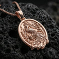 Load image into Gallery viewer, Rose gold plated peafowl necklace with detailed tail plumage, decorative floral branches, and elegant oval silhouette resting on volcanic rock in an elegant close-up product presentation