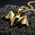 Load image into Gallery viewer, Gold plated origami bat pendant with geometric folded surfaces, pointed wing silhouette, and sleek nocturnal charm showcased on black volcanic rock in a refined macro jewelry image