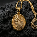 Load image into Gallery viewer, Gold plated owl pendant with detailed plumage, oval medallion silhouette, and symbolic bird of wisdom design showcased on black volcanic rock in a refined macro jewelry image