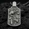 Load image into Gallery viewer, Oxidized swordfish pendant with detailed ocean life scene, swimming fish relief, and rectangular medallion silhouette displayed on dark volcanic rock in a close-up luxury jewelry composition