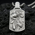 Load image into Gallery viewer, Polished silver swordfish necklace with sculpted marine predator, surrounding fish details, and elongated rectangular frame placed on textured volcanic rock in a premium studio product shot