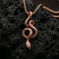 Load image into Gallery viewer, Rose gold plated serpent necklace with slender coiled snake design, detailed body texture, and elegant symbolic form resting on volcanic rock in an elegant close-up product presentation