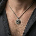Load image into Gallery viewer, Oxidized twin wolf pendant with howling and resting wolf design worn on the neck in a lifestyle jewelry shot, styled against the chest for a bold and wilderness-inspired statement look