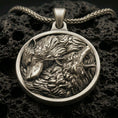 Load image into Gallery viewer, Bronze twin wolf pendant with flowing fur detail, howling and resting wolf relief, and round medallion silhouette displayed on dark volcanic rock in a close-up luxury jewelry composition