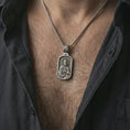 Load image into Gallery viewer, Oxidized Saint Peter dog tag pendant necklace worn on the neck, styled in a dark lifestyle portrait with an open shirt and masculine presentation.