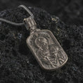Load image into Gallery viewer, Bronze Saint Paul dog tag pendant necklace with an oxidized finish resting on textured volcanic rock, captured in a close-up premium studio composition.